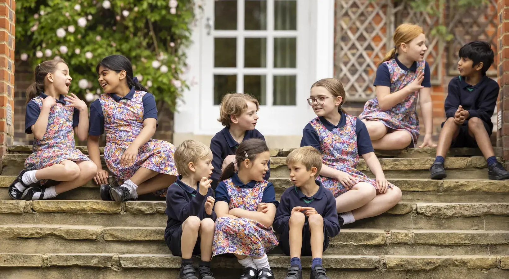 Ibstock Place School Prep pupils sitting on the main stairs of the schools, talking to each other.